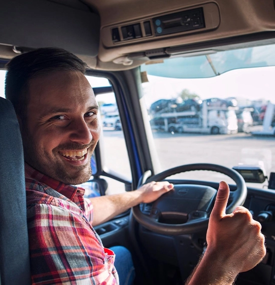 A truck driver sitting in his truck, holding a thumbs up